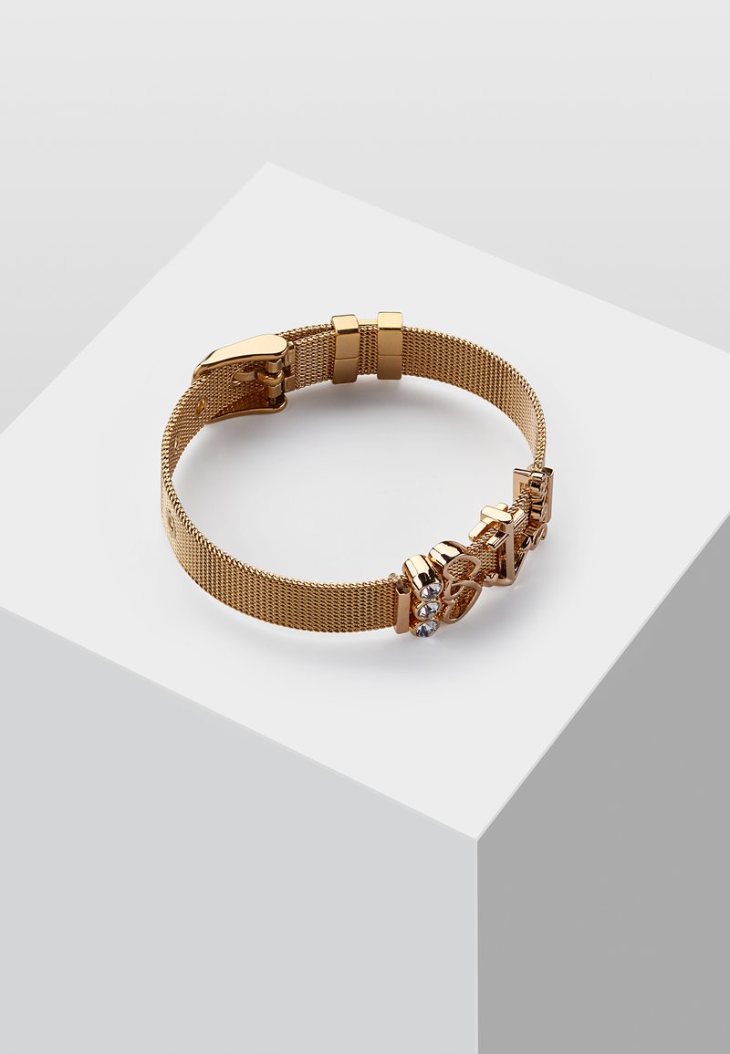 Il bracciale in rete dorata presenta un design con chiusura e accenti decorati, comprendente tre pietre trasparenti, mostrando una finitura elegante e texturizzata.