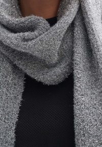 Écharpe gris clair en matière douce et texturée avec des fibres métalliques, disposée en boucle lâche autour du cou, sur un fond sombre.