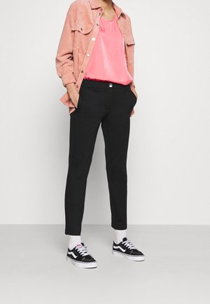 Zwarte tapered broek met een slim fit, gecombineerd met een felroze blouse en een koraalkleurig corduroy overhemd. Gedeeltelijk gedragen met zwart-witte sneakers.
