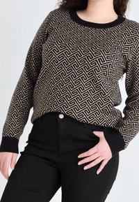 Pull noir et beige à motif avec design géométrique, col et poignets côtelés, associé à un pantalon noir ajusté.
