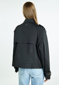 Zwarte jas met een cape-achtige rugontwerp, gemaakt van lichtgewicht materiaal, voorzien van lange mouwen en verstelbare manchetten.
