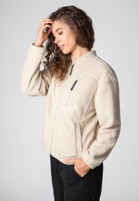 Beige Fleecejacke mit Reißverschlusstasche, strukturierter Stoff und Stehkragen. Verfügt über eine taillierte Passform und Seitentaschen.