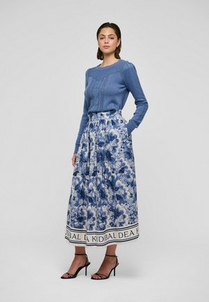 Sininen neulottu villapaita teksturoidulla kuviolla, yhdistettynä pitkään kukkakuviolliseen hameeseen, jossa on sinisiä ja valkoisia kuvioita sekä koristeellinen helma.