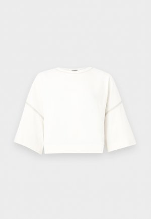 Λευκό cropped πουλόβερ με φαρδιές μανσέτες 3/4 και διακριτικές ραφές σε ανοιχτό γκρι φόντο.