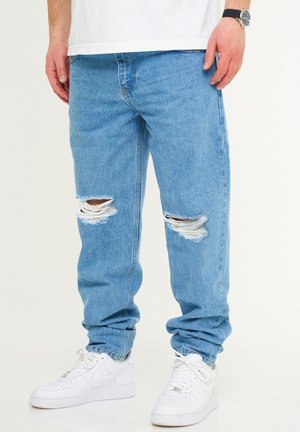 Hellblaue Jeans im Denim-Stil mit abgeriebenen Löchern an den Knien, lässiger Schnitt und schmal zulaufende Bündchen, kombiniert mit weißen Sneakers.
