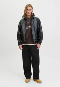 Sort faux læderjakke med høj krave, båret over en brun stribet t-shirt. Løse sorte bukser og lysebrune sko fuldender looks.