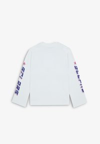 Camisa blanca de manga larga con texto y gráficos de estrellas en rosa y azul en la manga izquierda. Tela de algodón suave, corte relajado.