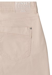 Beige pants with a back pocket and a label above it reading "SUNSET SHADES UNDER DESERT SKIES CECIL We love pants."