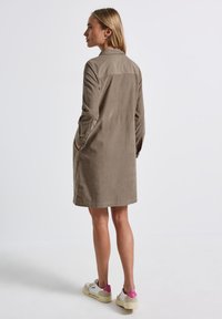 Beige knappad trenchcoat med rak silhuett, långa ärmar och sidofickor, kombinerad med vita sneakers med rosa detaljer.