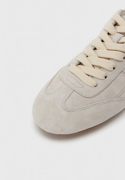 Ανδρικό αθλητικό παπούτσι από καστόρι σε ανοιχτό γκρι χρώμα με στρογγυλεμένη μυτερή μύτη, μπεζ κορδόνια και διακριτικές ραφές. Διαθέτει υφή στο επάνω μέρος και λεία σόλα.