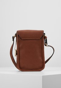 Piccolo borsa a tracolla in pelle marrone con chiusura a pattina e cinturino regolabile, posizionata su uno sfondo grigio chiaro uniforme.