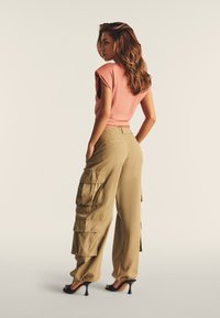 Pantaloni cargo color khaki con molte tasche, abbinati a una maglietta rosa a maniche corte aderente. L'outfit è completato da scarpe con tacco nere.