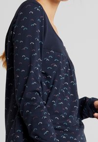 Mörkblå långt ärmad topp med rundad halsringning, prydd med små flerfärgade fläktmönster, mjukt material och en avslappnad passform.