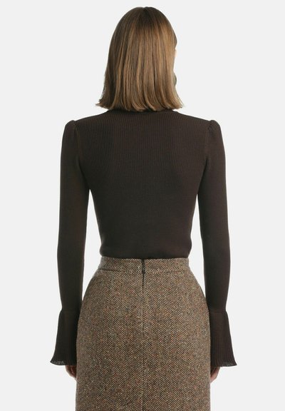 Brązowa, prążkowana bluzka z długim rękawem i rozszerzanymi mankietami, zestawiona z wysoko taliowaną spódnicą w rybią łuskę w ziemistych kolorach.
