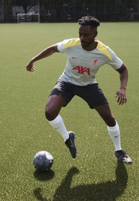 Liverpool FC jersey in grey with yellow accents and red branding, paired with black shorts, white socks, and black football shoes on artificial grass.
