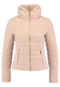 Veste beige matelassée avec col montant, fermeture éclair à l'avant avec tirette en anneau, et deux poches latérales zippées, silhouette ajustée avec couture horizontale.
