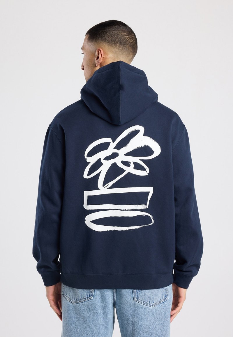 Marineblauwe hoodie met een wit grafisch ontwerp van een bloem en horizontale lijnen op de achterkant. Zacht katoenmateriaal en een ontspannen pasvorm.