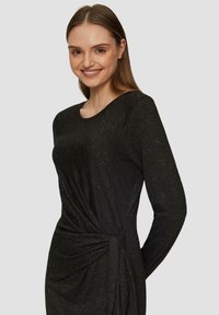 Schwarzes langärmliges Kleid mit Rundhalsausschnitt, das eine verdrehte Knotendetail an der Taille aufweist. Der Stoff hat eine zarte, schimmernde Textur.