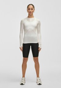 Vit långärmad träningslinne med nätinslag och svarta åtsittande shorts. Lätt och ventilerande material med tumhål i ärmarna.