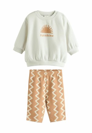 Pulover verde deschis cu imprimeu "soare" și manșete răsfrânte, asortat cu pantaloni bej cu model zigzag și talie elastică.