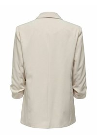 Blazer beige con texture liscia, forma strutturata, maniche a tre quarti arrotolate e un unico spacco sul retro per una maggiore libertà di movimento.