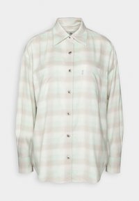 Camicia a scacchi con colletto in verde chiaro e beige. Presenta un colletto, maniche lunghe, due tasche sul petto e una vestibilità leggermente abbondante.