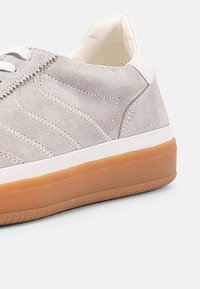 Lyse grå semsket sneakers med hvite detaljer, teksturert stikking og en såle av gummigummi. Lavskåret design med lisser og polstret krage.