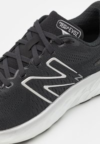 Černá sportovní obuv s prodyšným horním dílem z mesh materiálu, texturovaným povrchem, plochými tkaničkami a stříbrnými akcenty na straně. Polstrovaná bílá podrážka.