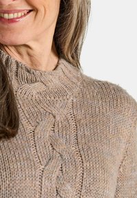 Pull en tricot dans des tons beiges avec un design en câble épais et un col côtelé, offrant un tissu doux et texturé.