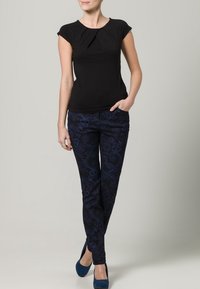 Svart kortärmad topp med plisseringsdetalj, parat med mörkblå byxor med en subtil virvelmönster och smal passform.