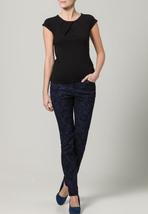 Top negro de manga corta con detalle de plisado, combinado con pantalones azul oscuro que presentan un sutil patrón de remolinos y un corte ajustado.