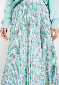 Fållad blommig kjol i ljusgrön, med lila och blå mönster. Mjuk tygstruktur med en flödande design och mellanhöjd.