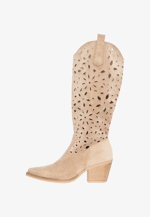 Botte cowboy en daim beige avec des motifs découpés floraux, talon empilé en bois et bout légèrement pointu.