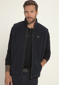 Gilet in pile di un blu navy scuro con zip frontale, due grandi tasche anteriori e un piccolo logo sul lato sinistro in alto. Texture liscia.