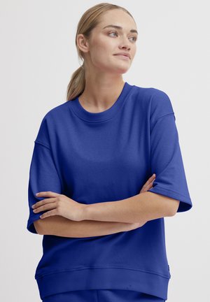 Sweatshirt bleu royal à manches courtes en tissu doux avec un col et un ourlet côtelés, présentant une coupe décontractée et des détails sur les côtés.