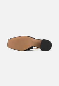 Semelle de chaussure en tissu noir tissé avec un fond beige tanné et texturé. Bout carré et design à talon minimal. Bords lisses et accents discrets.