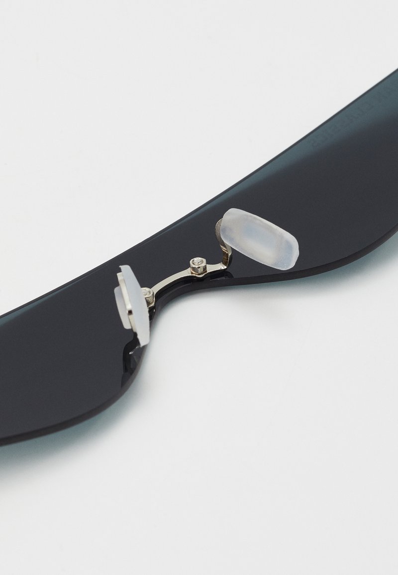 Ochelari de soare negri cu un cadru neted, balama metalică și tamponi nazali din silicon transparent pentru confort. Design lustruit cu detalii minime.