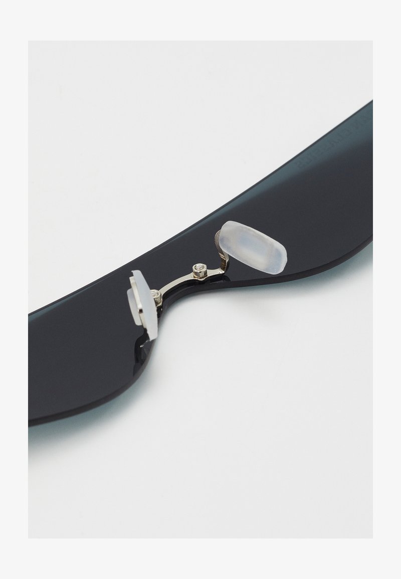 Ochelari de soare negri cu un cadru neted, balama metalică și tamponi nazali din silicon transparent pentru confort. Design lustruit cu detalii minime.