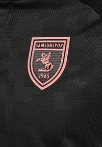 Svart sportströja med texturerad tyg. Har en rosa sköldlogotyp med texten "SAMSUNSPOR" och "1965" samt en hästdesign.