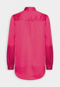 Blouse rose en satin à manches longues avec poignets boutonnés, une empiècement dans le dos et un pli central au dos, vue de dos sur fond blanc.