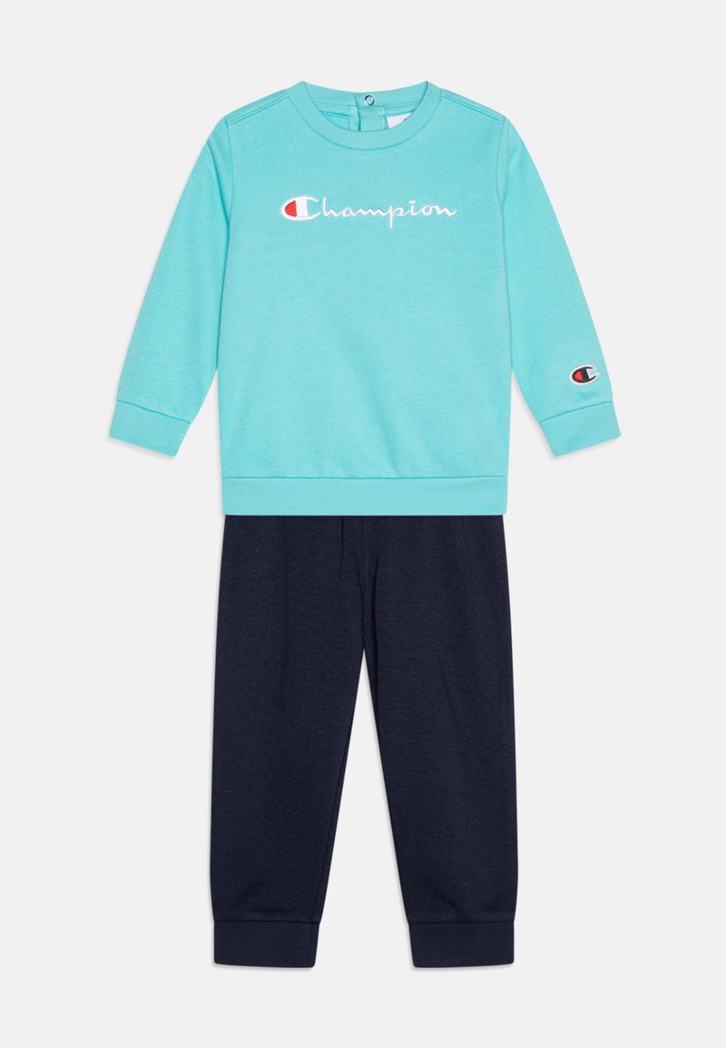 Felpa turchese con ricamo 'Champion' e pantaloni della tuta blu marino. Presenta polsini a coste e una texture di tessuto morbido. Collo rotondo.