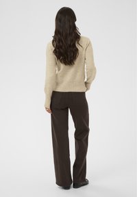 Suéter de punto beige con mangas largas, combinado con pantalones de pierna recta marrón oscuro. Textura suave y sutiles acentos acanalados en el dobladillo.