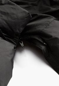 Black insulated jacket with a smooth texture and zipper detail. Features a high collar and stitched panels for added warmth.