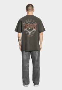 Ciemnoszary oversize t-shirt z graficznym nadrukiem "ATHLETIC 1999" i wzorem piłki na plecach; w połączeniu z szarą dżinsową spodnią.