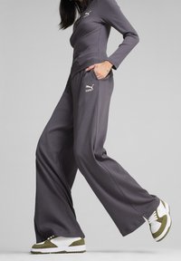 Ensemble athlétique gris côtelé comprenant un haut à manches longues et un pantalon ample, assorti à des baskets blanches et vert olive. Logo visible sur la poitrine et le pantalon.