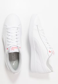 Zapatillas deportivas blancas con parte superior sintética, lengüeta acolchada y detalles en gris. Cuentan con una suela de goma texturizada y detalle de logotipo rosa.