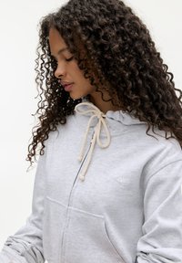 Lichtgrijze sweatshirt met een capuchon en beige trekkoorden, met een voorzak en subtiele geborduurde details op de borst.