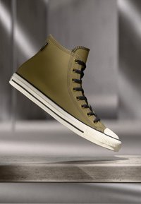 Adidași înalți din cauciuc verde măslinie cu șireturi negre, talpă din cauciuc alb și vârf. Prezintă cusături contrastante și un design elegant.