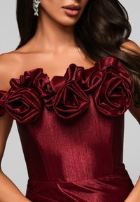 Burgundowa sukienka z odkrytymi ramionami, zdobiona trzema dużymi aplikacjami w kształcie satynowych róż oraz gładką, błyszczącą fakturą. Dopasowana góra z talią podkreśloną.