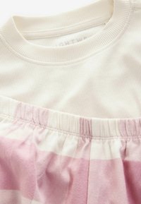 Top in tessuto a costine bianco con scollatura rotonda, abbinato a una gonna a scacchi rosa e bianca con vita elasticizzata. Texture morbida visibile.